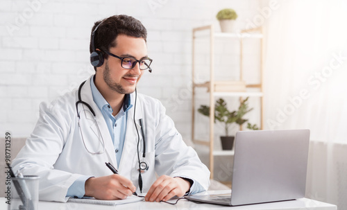 Online lessons and conferences. Doctor makes notes sitting at table with laptop in interior, free space