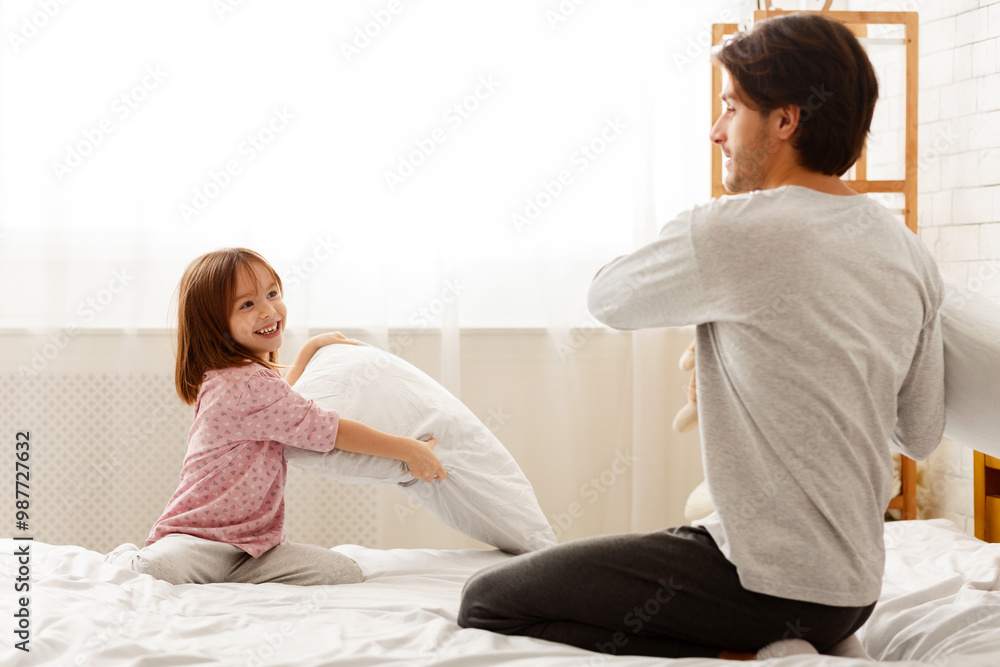 Little daughter and young dad having pillow fight together in bedroom, empty space Little daughter and young dad having pillow fight together in bedroom, empty space