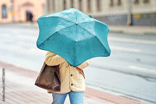 Woman with turquoise umbrella, strong wind blowing. Female holding turquoise umbrella during thunderstorm. Woman strugle with wind. Person with umbrella hiding from strong stormy wind, rain.