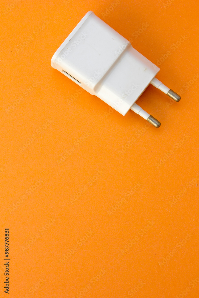 A white power adapter on an orange background provides a modern and dynamic feel, perfect for illustrating concepts of energy supply. A white power adapter on an orange background provides a modern and dynamic feel, perfect for illustrating concepts of energy supply.