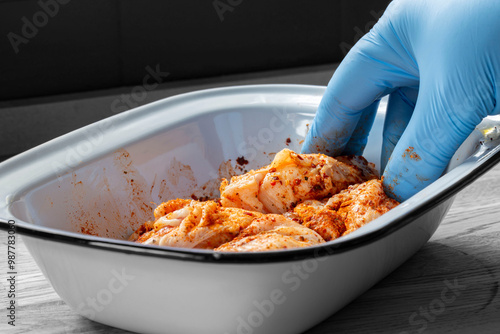 Person seasoning raw chicken with hot thai bbq seasoning in an enamal dish. Food preparation concept. photo