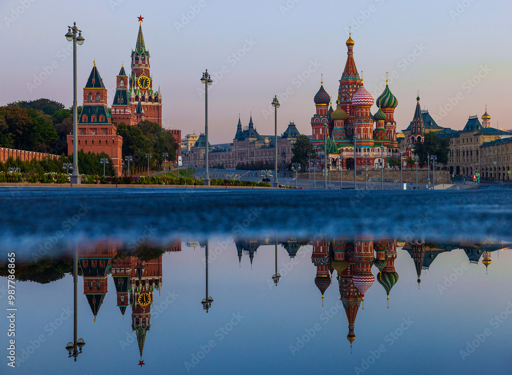Fototapeta premium Twilight casts a beautiful glow on St. Basil's Cathedral and the Kremlin as they reflect in calm water in Red Square, showcasing Moscow's stunning architecture and historical significance at dusk.