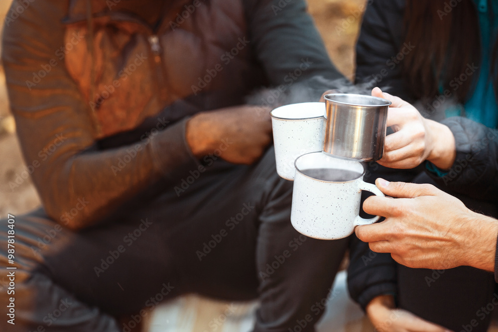 Warming up in camping. Hands of international hikers cheering up with camping cups, camping in forest, closeup Warming up in camping. Hands of international hikers cheering up with camping cups, camping in forest, closeup