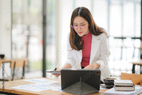 Focused and Determined: A young businesswoman in a modern office setting, intently studying data on her tablet. She exudes confidence and professionalism as she analyzes charts and graphs, showcasing 