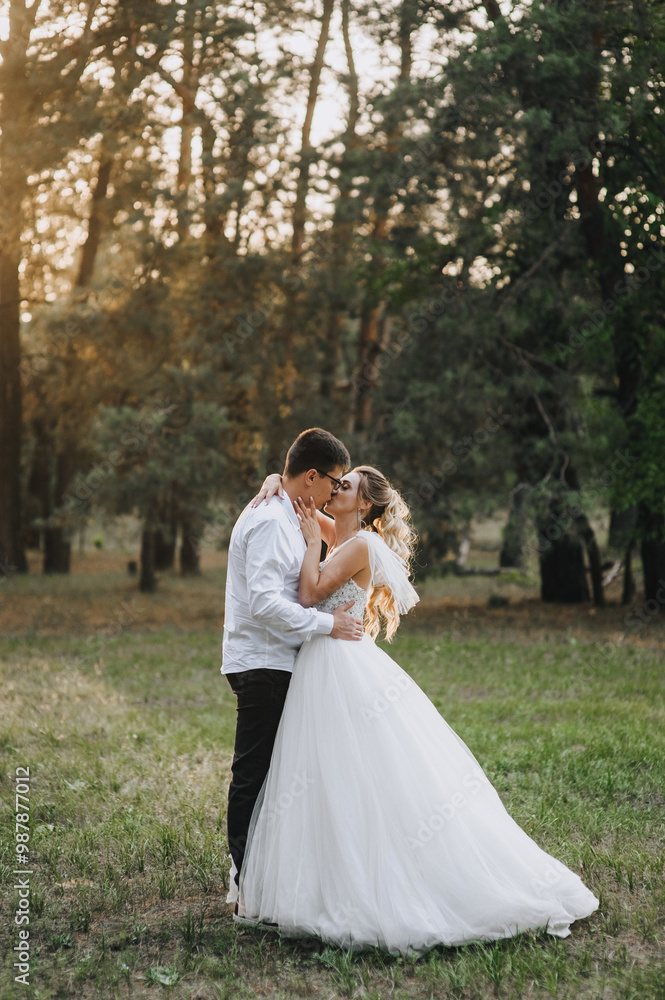 Fashionable groom and beautiful smiling bride curly blonde in white long dress hugging kissing outdoors in forest in nature evening at sunset. Wedding photography, portrait of happy newlyweds. Fashionable groom and beautiful smiling bride curly blonde in white long dress hugging kissing outdoors in forest in nature evening at sunset. Wedding photography, portrait of happy newlyweds.