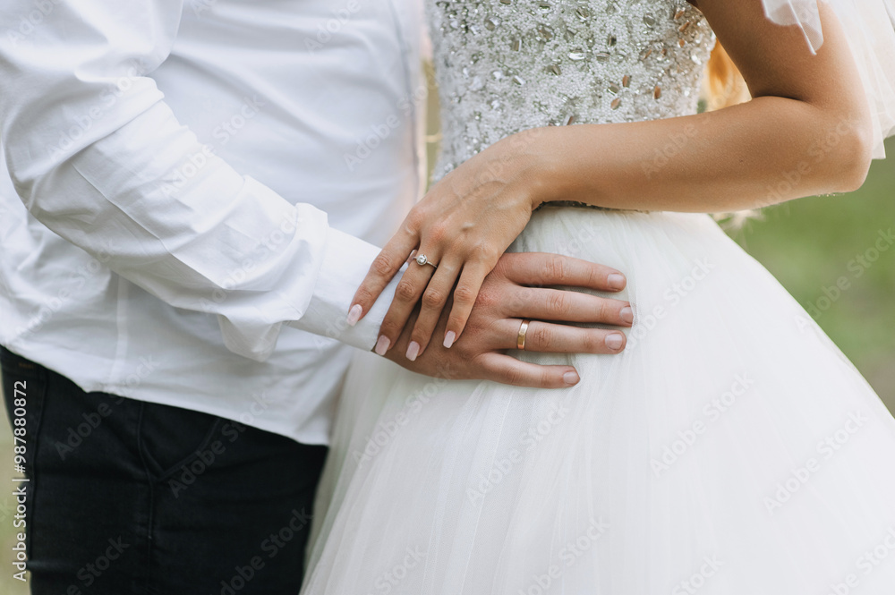Groom in white shirt with bracelet and bride in dress with gold ring on finger standing outdoors holding hands. Close-up wedding photo of happy newlyweds. Groom in white shirt with bracelet and bride in dress with gold ring on finger standing outdoors holding hands. Close-up wedding photo of happy newlyweds.