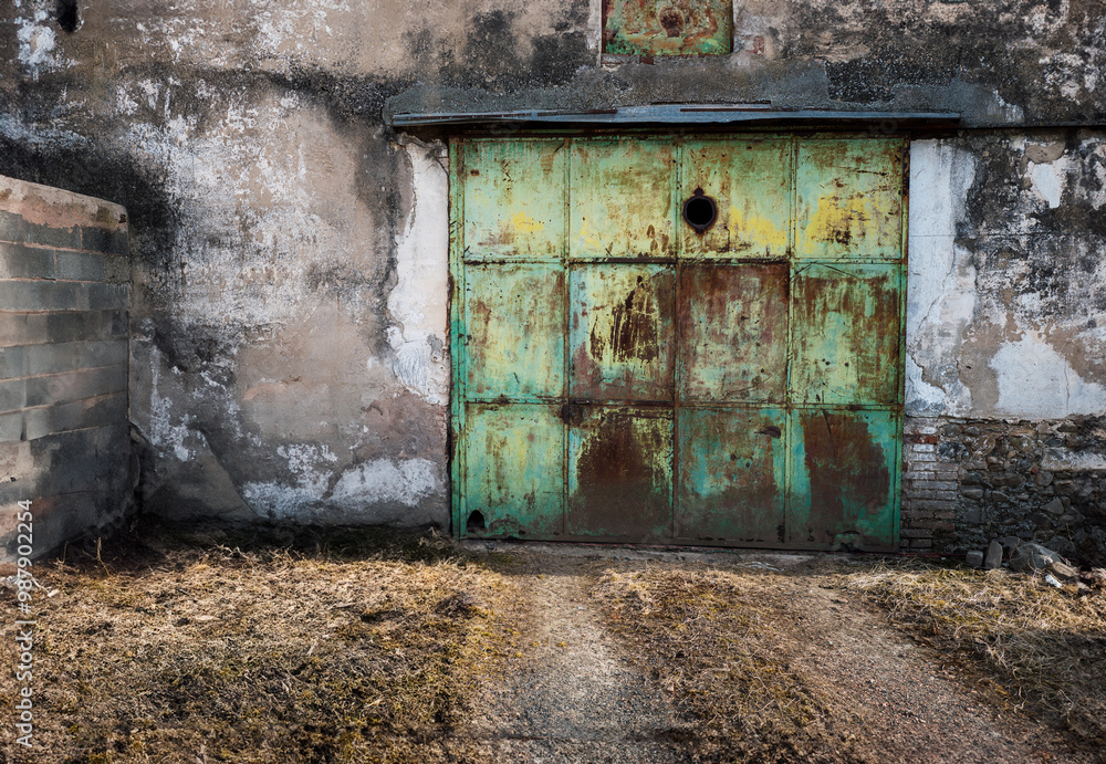 A large, weathered metal door with rusted patches is set in a distressed concrete wall, surrounded by a rough, grassy area. A large, weathered metal door with rusted patches is set in a distressed concrete wall, surrounded by a rough, grassy area.