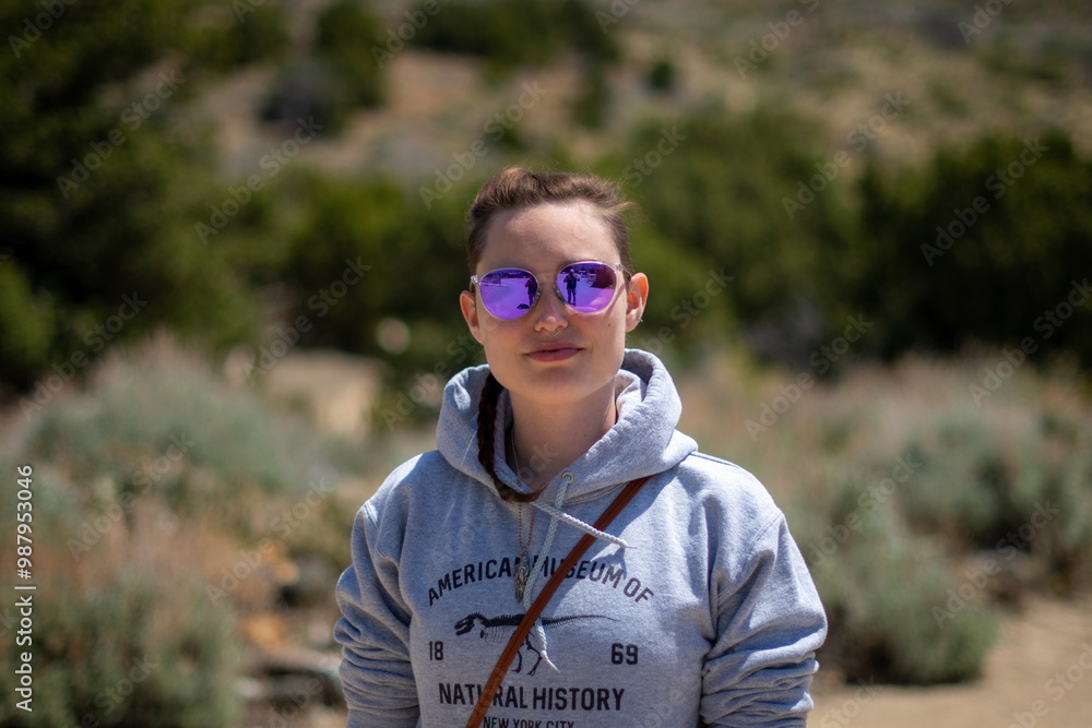 portrait of a person in bright sun outdoors with purple glasses, gray sweater with hill in the background. portrait of a person in bright sun outdoors with purple glasses, gray sweater with hill in the background.