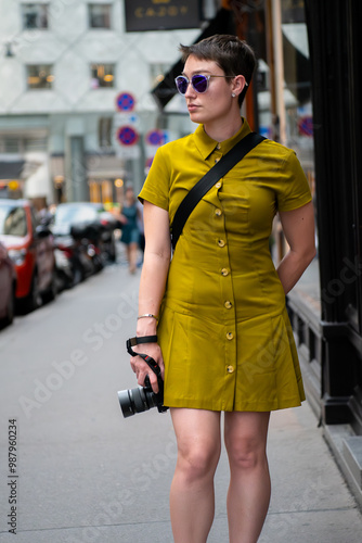 woman walking on the street in a green dress holding a camara, looking away.