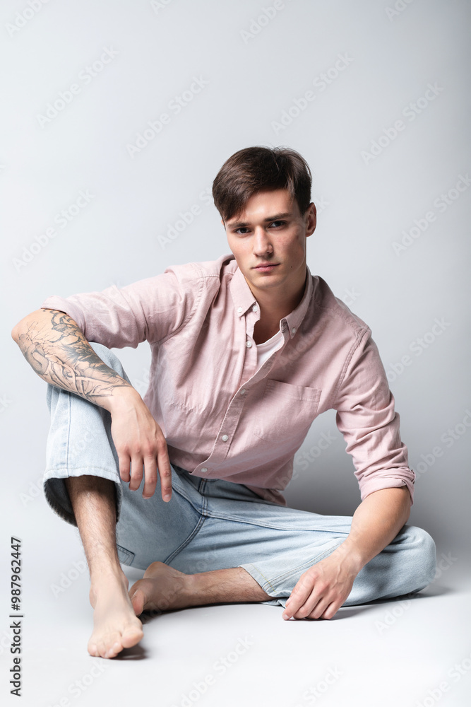 Male portrait on a studio background. A young guy in blue jeans and a shirt. Model looking guy Male portrait on a studio background. A young guy in blue jeans and a shirt. Model looking guy
