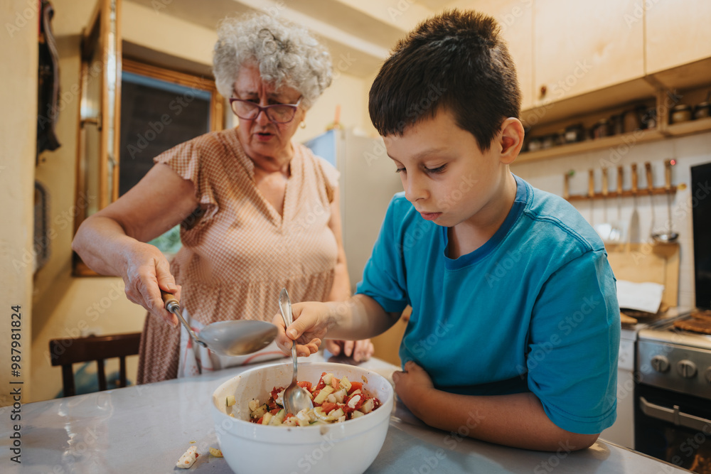 A grandmother and her grandson are seen working together in the kitchen, preparing a meal. The image captures a loving family interaction and the tradition of cooking. A grandmother and her grandson are seen working together in the kitchen, preparing a meal. The image captures a loving family interaction and the tradition of cooking.