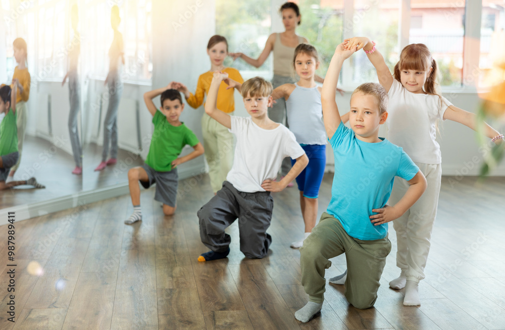 Fototapeta premium Joyous little boy and girl training waltz poses together with other attendees of dancing courses