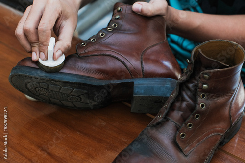 Cuadro en lienzo Close up of a hands polishing a leather boots with mink oil with sponge, on wooden table, shoes shining and cleaning