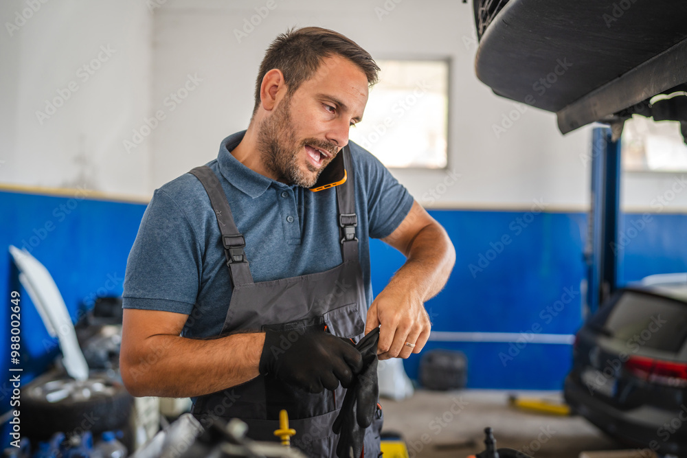 Car mechanic work on engine while talk on mobile phone in garage Car mechanic work on engine while talk on mobile phone in garage