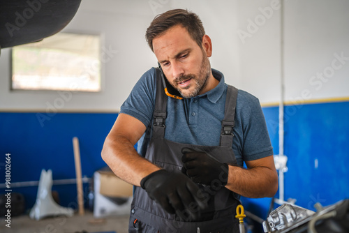 Car mechanic work on engine while talk on mobile phone in garage