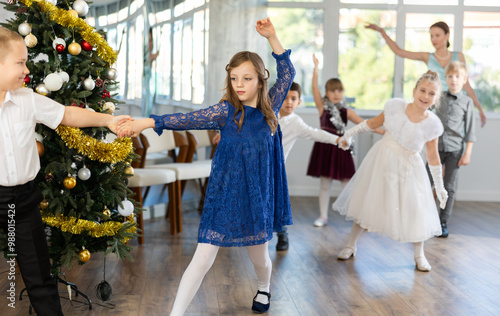 Joyful minor schoolboys and schoolgirls training valse dance in events salon adorned with Xmas tree photo