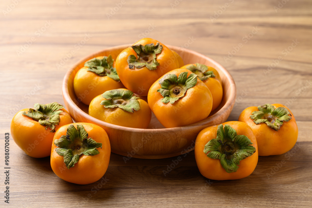 Ripe persimmon fruit in wooden bowl on wooden background Ripe persimmon fruit in wooden bowl on wooden background
