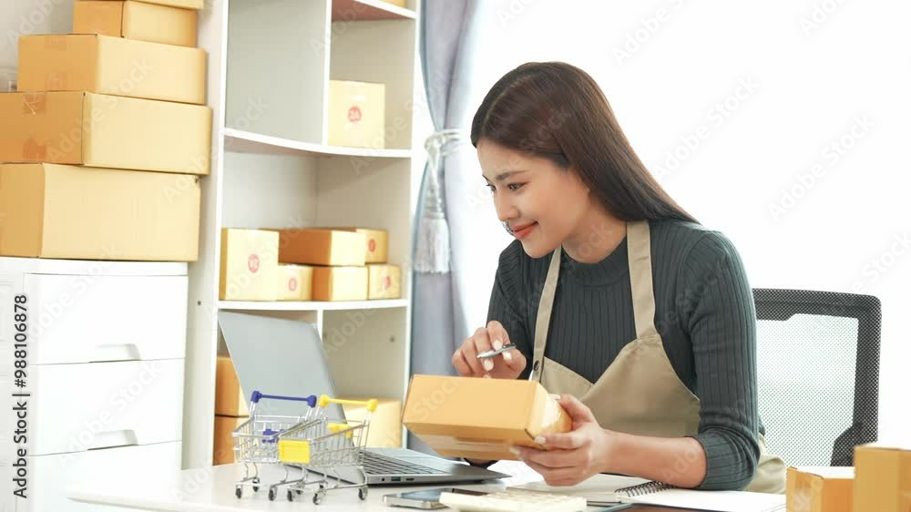 Female SME business owner entrepreneur working on receipt boxes and checking online orders to prepare to pack boxes, sell to customers. Online SME business concept, small business startup.