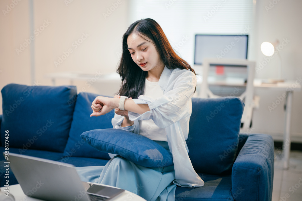 Young asian woman is sitting on a blue sofa in her home office ...