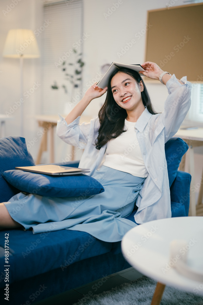 Young woman relaxes at home, sitting on her sofa with a book, smiling ...