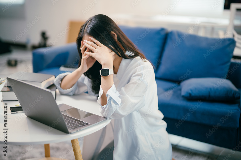 © Parichat - Young asian woman is experiencing stress and burnout while working from her home office. She is holding her head in her hands, feeling overwhelmed by the demands of her work