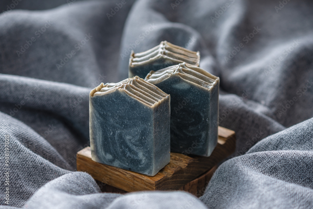 Natural black and white handmade soap on a wooden soap dish on a background of gray fabric Natural black and white handmade soap on a wooden soap dish on a background of gray fabric