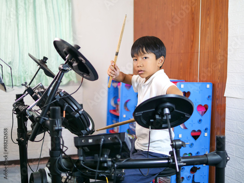 Asian child boy hold drumstick to play electronic drum with happy smiling face at home. Concept of music learning, happy relaxing time, freedom, little kid musician.

