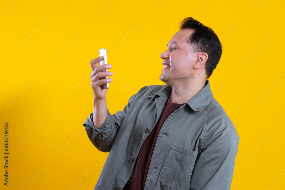 Side view of happy Asian man using smartphone reading good news message or enjoying mobile application. Side view of happy Asian man using smartphone reading good news message or enjoying mobile application.