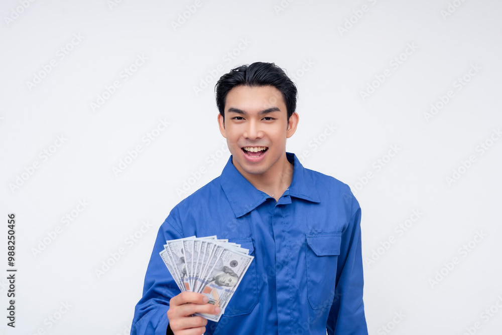 Smiling young construction worker in blue coveralls holding hundred dollar bills, isolated on white background, symbolizing financial success and well paying job. Smiling young construction worker in blue coveralls holding hundred dollar bills, isolated on white background, symbolizing financial success and well paying job.