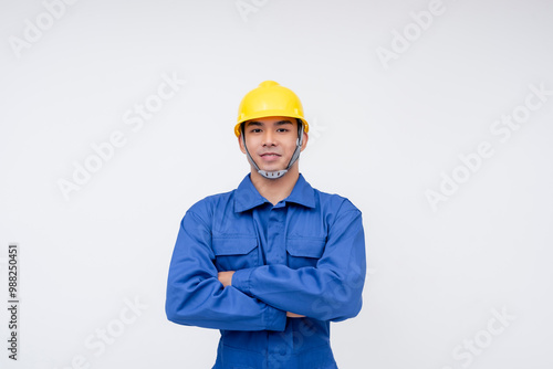 Confident young construction worker wearing blue coveralls and a yellow hard hat, standing against a white background, embodying professionalism and safety.