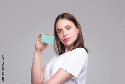 Young woman in white t-shirt holding credit card near face, isolated over gray background. Pay wit credit or debit card. Bank card. Plastic credit card.