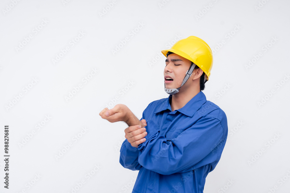 Young male construction worker in blue coveralls holding his injured wrist. Safety risks and work-related injury concept on a white background. Young male construction worker in blue coveralls holding his injured wrist. Safety risks and work-related injury concept on a white background.