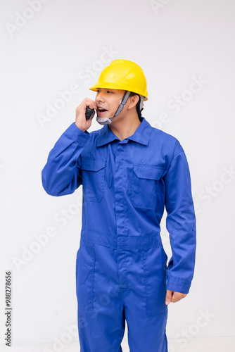 A young construction worker wearing blue coveralls and a yellow hard hat, using a two-way radio on a white background.