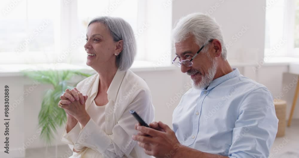 Excited gray haired senior elderly couple sitting together, holding remote controller, watching football on TV at home. Wife and husband supporting sport team, happily smiling and celebrating goal. Excited gray haired senior elderly couple sitting together, holding remote controller, watching football on TV at home. Wife and husband supporting sport team, happily smiling and celebrating goal.