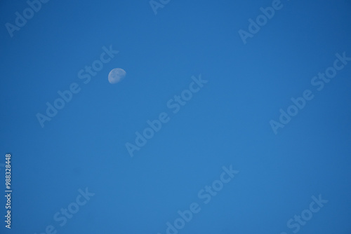 A clear blue sky with the moon visible during daylight hours in early afternoon