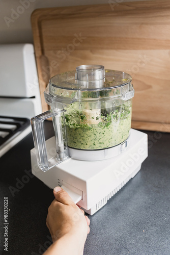 Person blending pesto ingredients in a food processor on a counter photo