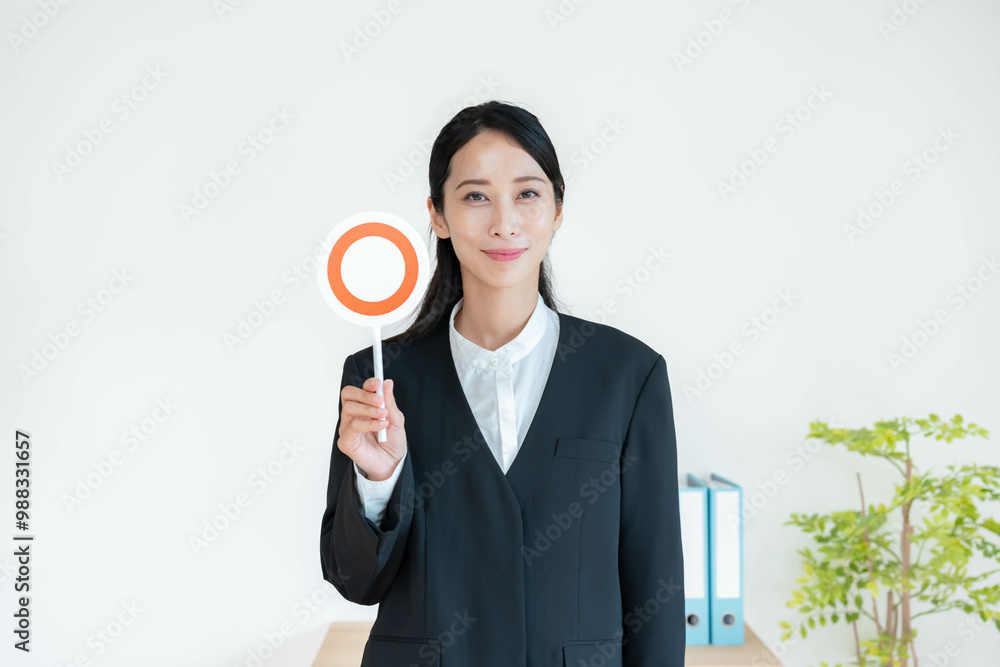 マルの札を持つスーツを着た女性