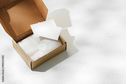 Fototapeta Naklejka Na Ścianę i Meble -  Brown cardboard box with a blank envelope on a light background in a well-lit setting