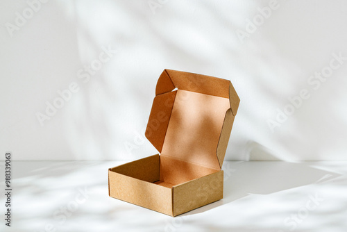 An open cardboard box rests on a bright white surface with soft shadows highlighting its edges and structure in natural light