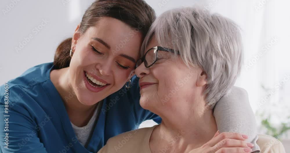 Nurse tenderly hugs elderly female patient and shows deep sense of compassion and care for her. Young medical worker cheerfully talks to elderly patient and gives her emotional support. Close up. Nurse tenderly hugs elderly female patient and shows deep sense of compassion and care for her. Young medical worker cheerfully talks to elderly patient and gives her emotional support. Close up.