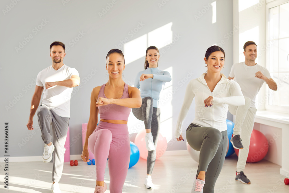 Naklejka premium Group of fit and active group of sporty people doing sport exercises in gym. Happy smiling men and women in sportswear having workout indoors together. Sport training, exercising and fitness concept.