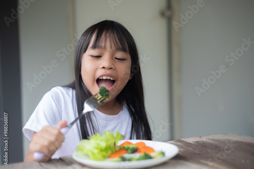 A young girl is eating a plate of vegetables, including broccoli and carrots