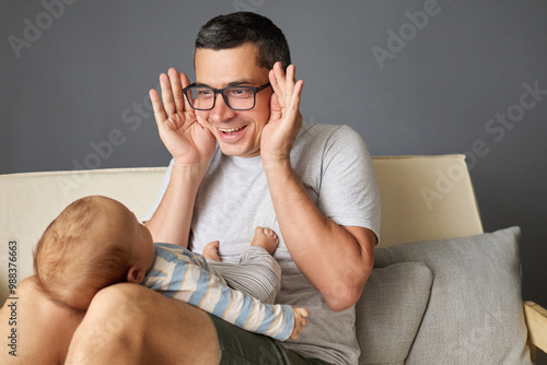 Tableau sur toile Dad playing peekaboo with his newborn daughter or son while sitting on sofa in l
