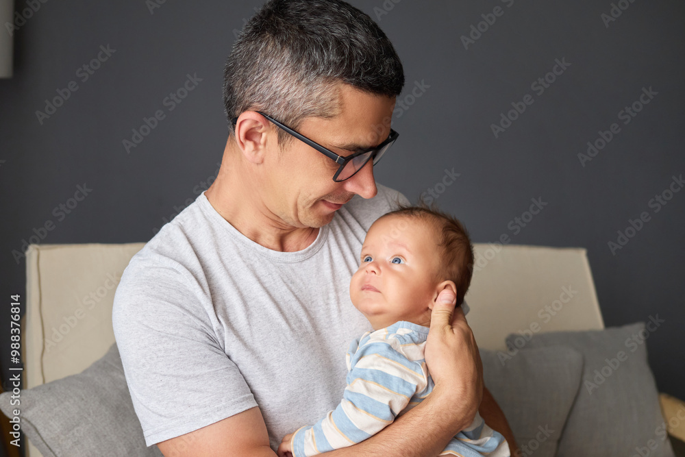 Handsome Caucasian dad holding newborn daughter smiling and caring for baby enjoying precious childhood moments while caring for newborn son sitting on couch Handsome Caucasian dad holding newborn daughter smiling and caring for baby enjoying precious childhood moments while caring for newborn son sitting on couch