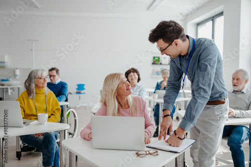 Teacher explaining senior students how to work with laptop and internet. Elderly people attending computer and technology education class. Digital literacy.