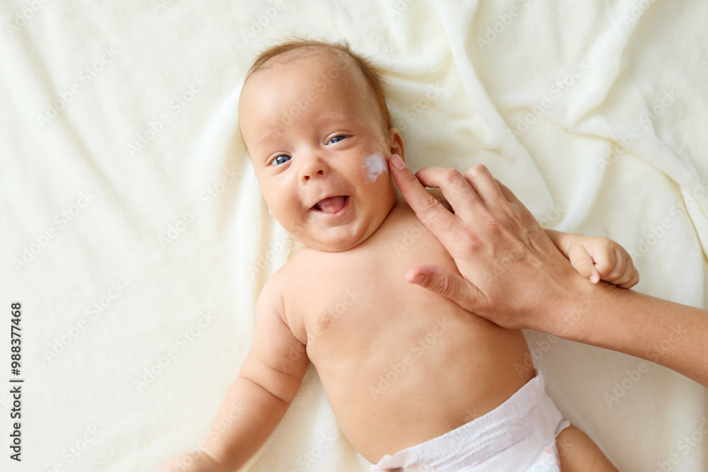 Mother applying lotion to her newborn’s cheeks with gentle hands ensuring the baby’s skin staying moisturized and healthy doing her daily care routine Mother applying lotion to her newborn’s cheeks with gentle hands ensuring the baby’s skin staying moisturized and healthy doing her daily care routine