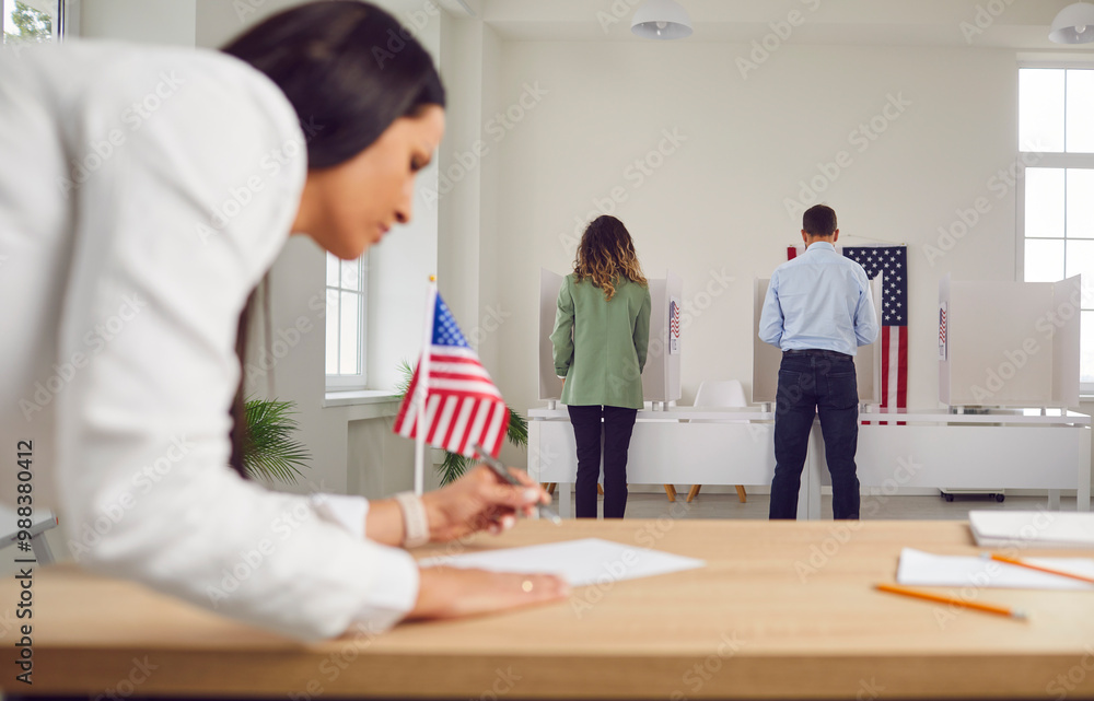 Fototapeta premium Young woman employee work in voting center. People american voters voting standing back in a row at vote center with USA flags in polling booth. Election day and democracy concept.