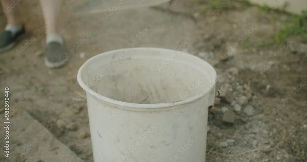 Handheld shot of a female using a shovel to collect dirt. Putting the dirt into a white bucket. Cleaning the garden after renovating.