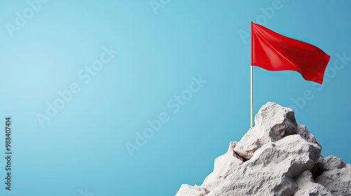 A vibrant red flag proudly waves atop a rocky peak against a clear blue sky, symbolizing achievement and ambition.