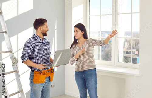 Young woman talking to a repairman who is going to make repairs in her house. Workman with a tool belt and laptop listening a girl homeowner explaining to him what work she needs to done at home photo